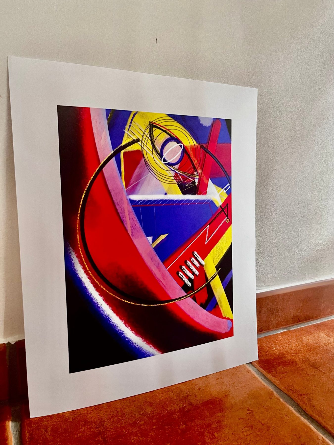 Print of a red, pink, blue and yellow painting leaning against a wall on a terracotta floor